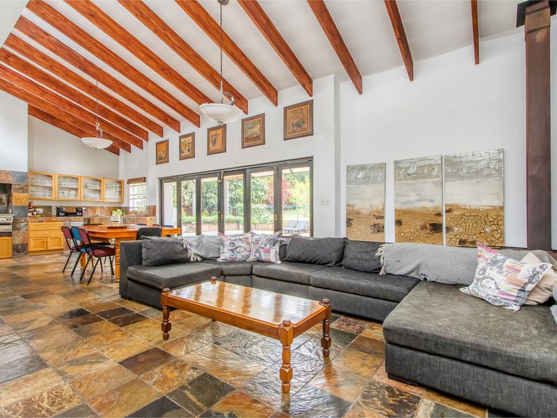 Spacious open-plan living and kitchen area featuring high vaulted ceilings with exposed timber beams, slate flooring, and large sliding doors leading to the garden.
