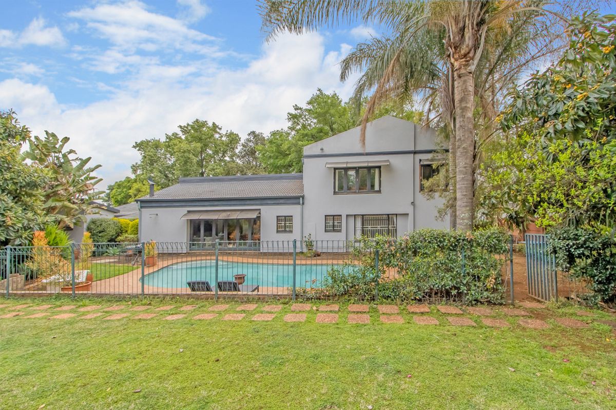 Rear view of the property featuring a swimming pool, paved surround, metal fencing, and a well-maintained garden area.