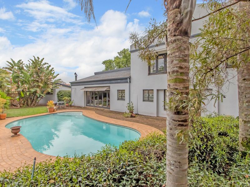 A well-maintained rear garden featuring a swimming pool with brick paving, a retractable awning over the patio, and established landscaping.