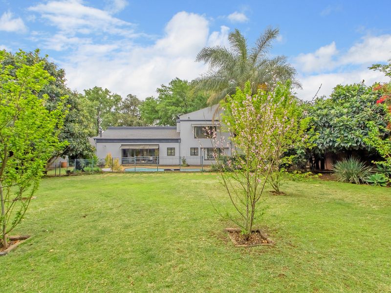 A spacious rear garden featuring a well-maintained lawn, mature trees, and a swimming pool with safety fencing, providing a private outdoor living space.