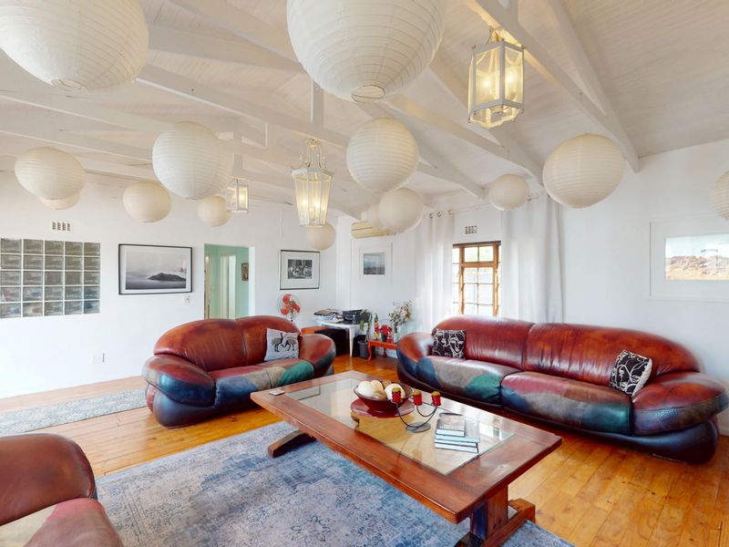 Spacious living room featuring exposed white timber beams, warm hardwood flooring, and a unique glass block window feature, creating a bright and airy atmosphere.