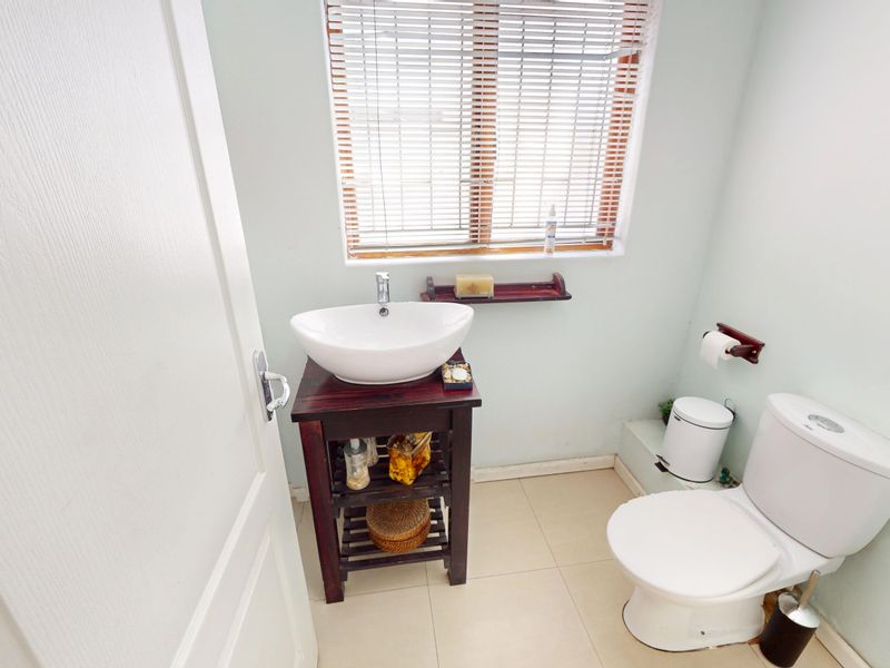A compact bathroom featuring a vessel sink on a wooden vanity, a standard toilet, and tiled flooring with natural light from a window.