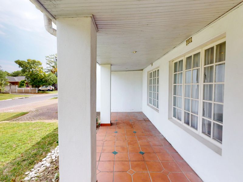 A covered front patio featuring tiled flooring, structural columns, and multi-pane windows, providing a sheltered entrance area.