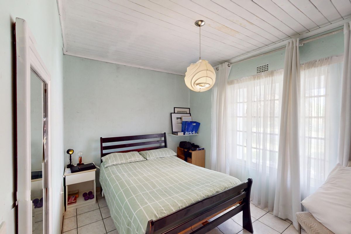 A bedroom featuring tiled flooring, a timber plank ceiling with visible water staining, and a large window allowing natural light.