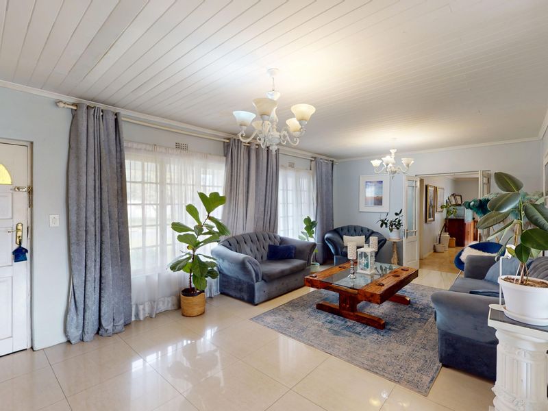 Spacious living room featuring tiled flooring, a timber panelled ceiling, and classic chandelier lighting, offering a bright and welcoming atmosphere.