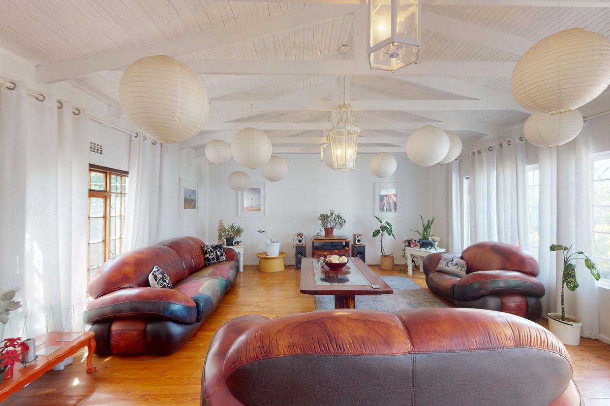Spacious living room featuring exposed timber ceiling beams, warm timber flooring, and large windows that provide ample natural light.