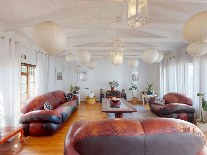 Spacious living room featuring exposed timber ceiling beams, warm timber flooring, and large windows that provide ample natural light.