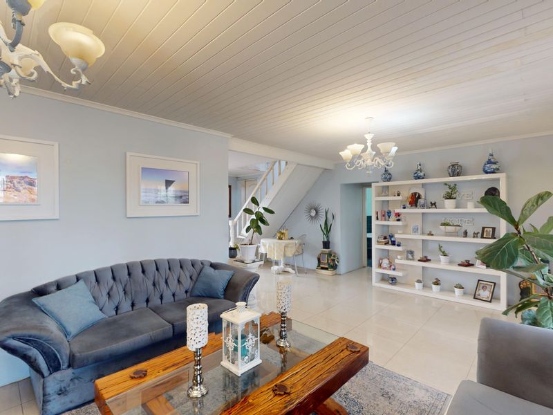 Spacious living room featuring tiled flooring, a tongue and groove ceiling, and a built-in shelving unit, with an open staircase leading to the upper level.