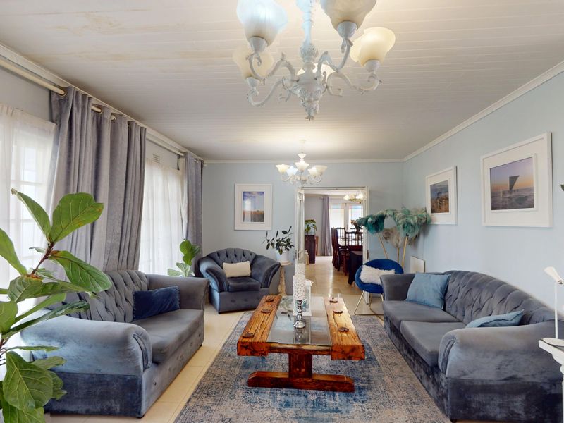 Spacious living room featuring a timber panelled ceiling, chandelier lighting, and tiled flooring, with direct access to the exterior through sliding glass doors.
