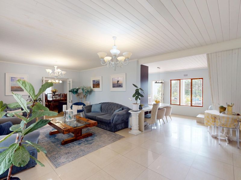 Spacious open-plan living and dining area featuring tiled floors, a timber panelled ceiling, and elegant chandelier lighting, creating a bright and inviting atmosphere.