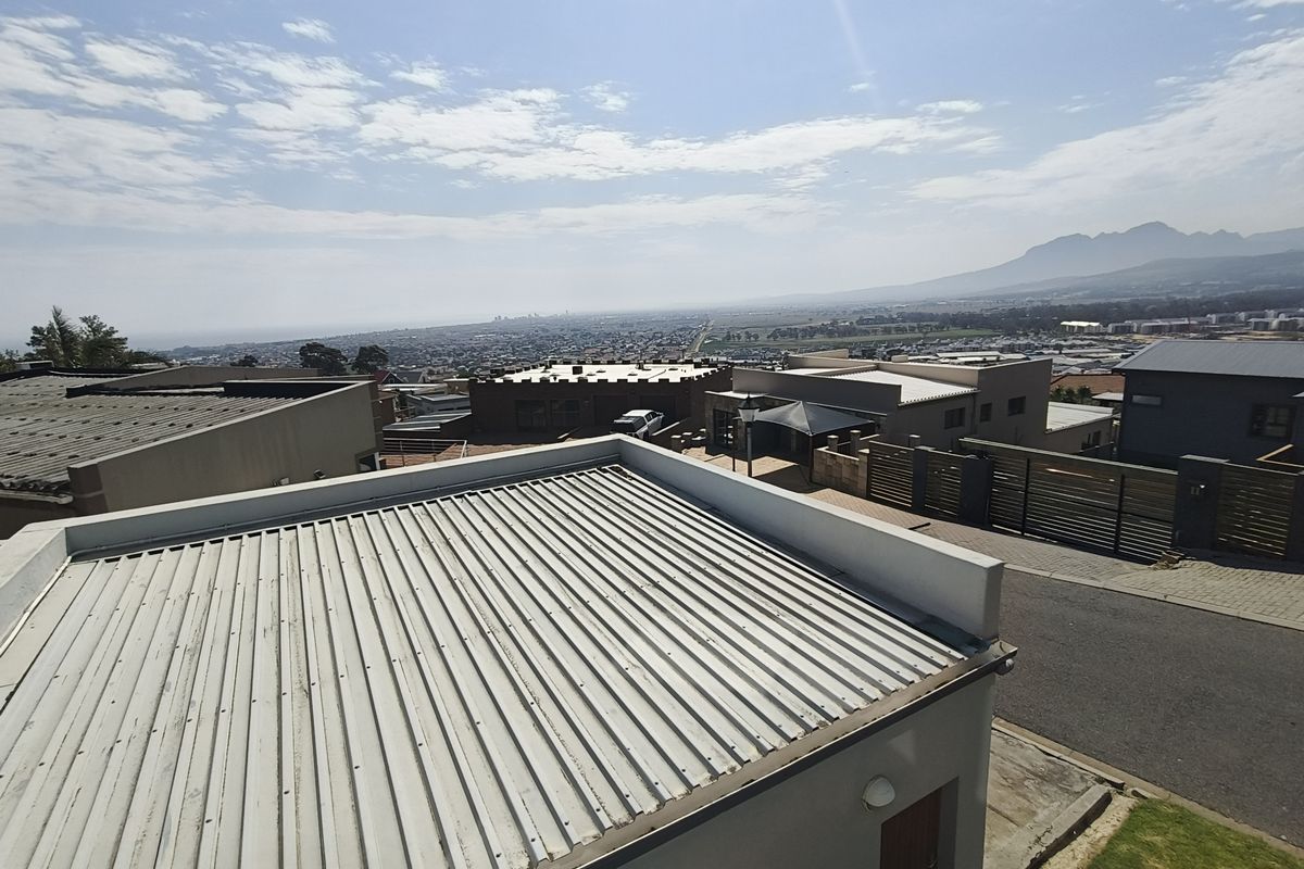 An elevated aerial view showing the property's corrugated metal roof, surrounding neighborhood, and distant mountain landscape.