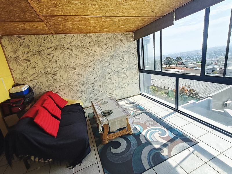 A sunlit living area featuring large floor-to-ceiling windows with expansive views, tiled flooring, and a unique textured ceiling finish.