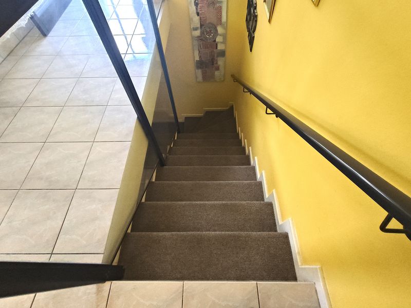 A staircase featuring carpeted steps, a black metal handrail, and tiled flooring at the landing.
