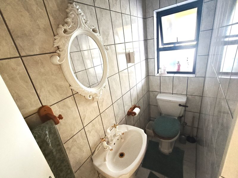 A compact bathroom featuring full-height ceramic wall tiling, a pedestal basin with vintage-style taps, and a standard toilet.