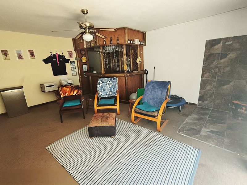 A dedicated bar area featuring a built-in wooden bar counter, ceiling fan, and a tiled fireplace hearth, offering potential for a modern entertainment space.