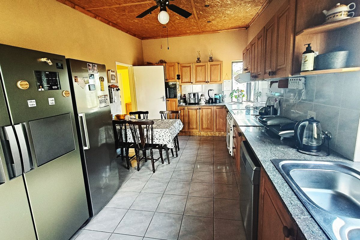 A functional kitchen featuring wooden cabinetry, granite countertops, tiled flooring, and a ceiling fan, with an integrated dining area.