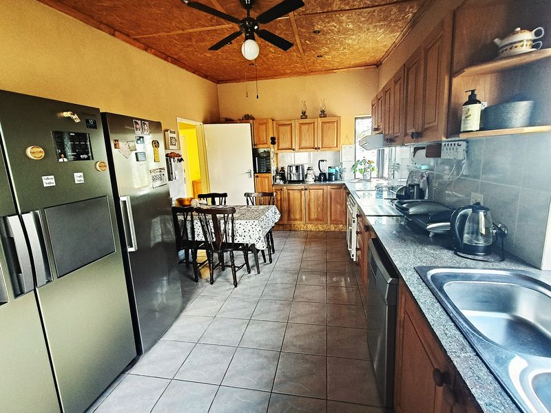 A functional kitchen featuring wooden cabinetry, granite countertops, tiled flooring, and a ceiling fan, with an integrated dining area.
