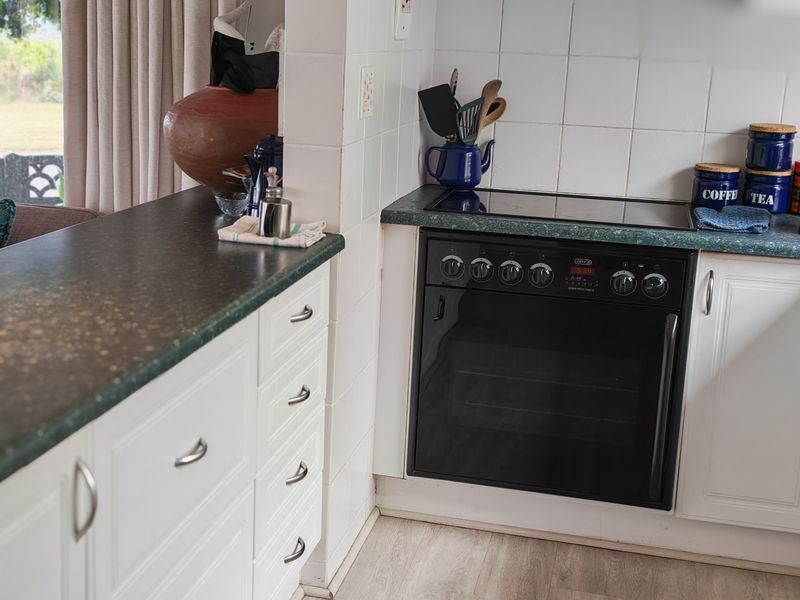 A functional kitchen area featuring white cabinetry, dark laminate countertops, a built-in oven, and an electric hob with a tiled splashback.