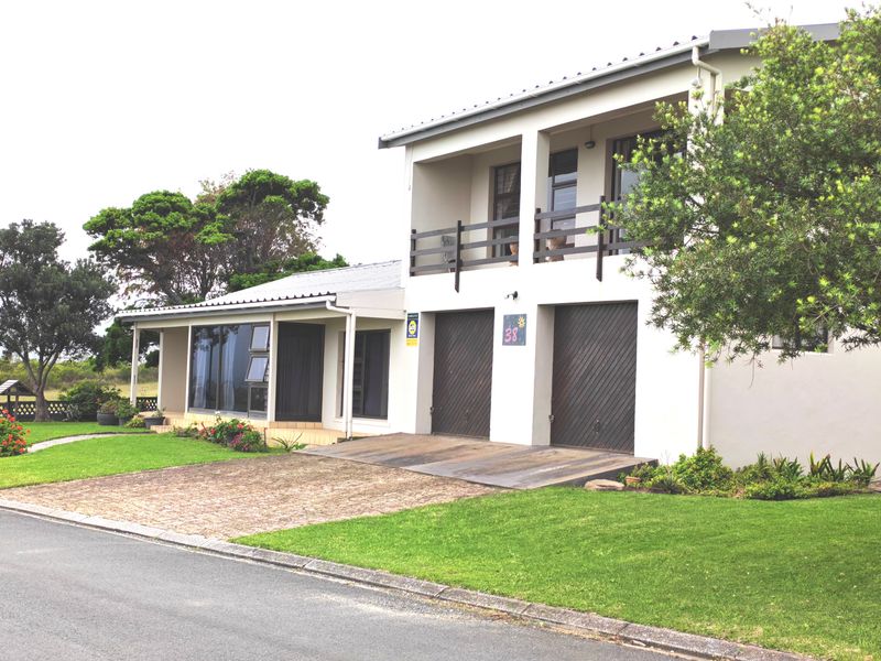 Front elevation of a two-story house featuring a double garage, paved driveway, and an upper-level balcony with a well-maintained garden.