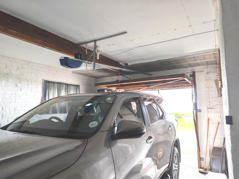 A functional garage space featuring exposed timber beams, painted brick walls, and an automated garage door mechanism.