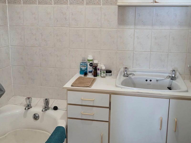 A dated bathroom featuring a built-in vanity with a ceramic basin, a bathtub, and full-height wall tiling.