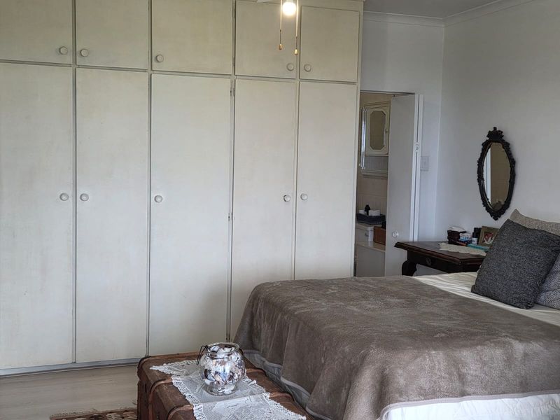 A bedroom featuring extensive floor-to-ceiling built-in cupboards, a ceiling fan, and laminate flooring, with an adjacent en-suite bathroom visible.