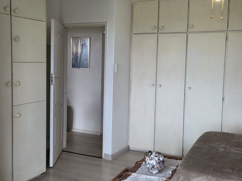 Bedroom featuring extensive built-in cupboards and light-toned laminate flooring, offering a functional space with potential for cosmetic updates.