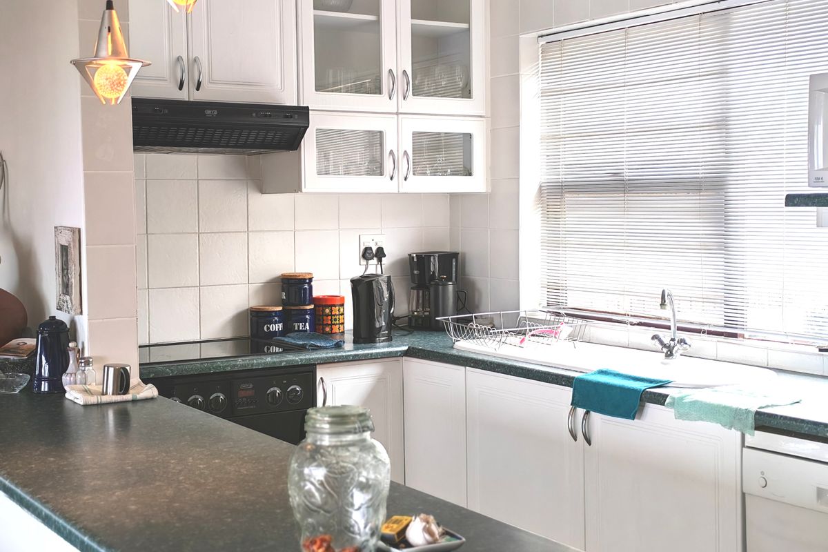 A functional kitchen featuring white cabinetry, dark laminate countertops, a built-in electric hob and oven, and a tiled backsplash with natural light.