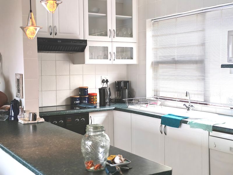 A functional kitchen featuring white cabinetry, dark laminate countertops, a built-in electric hob and oven, and a tiled backsplash with natural light.