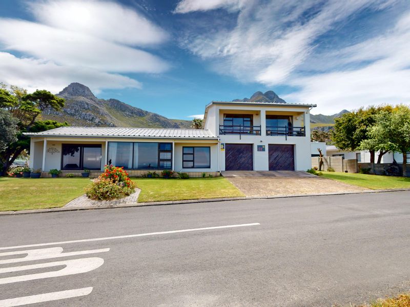 A well-maintained two-story house featuring a double garage, upper-level balcony, and expansive windows, set against a scenic mountain backdrop.