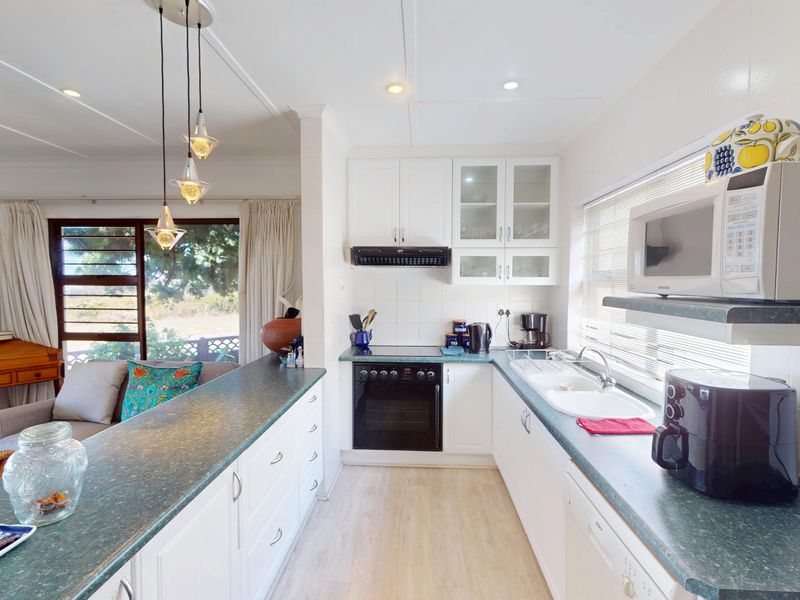 An open-plan kitchen featuring white cabinetry, laminate countertops, and integrated appliances, seamlessly flowing into the adjacent living area with natural light.