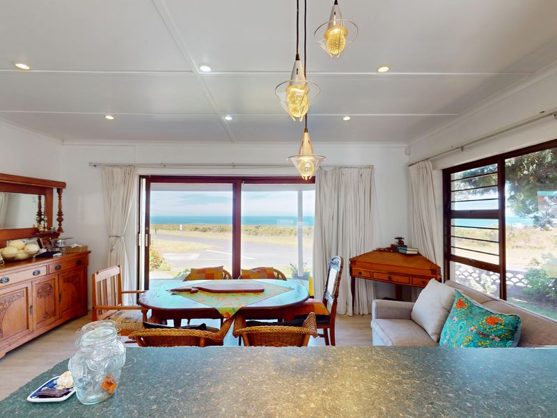 Open-plan living and dining area featuring large sliding doors with ocean views, recessed lighting, and a stone-look kitchen counter.