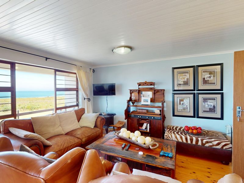 A comfortable living room featuring timber flooring, a tongue and groove ceiling, and a large window offering scenic coastal views.