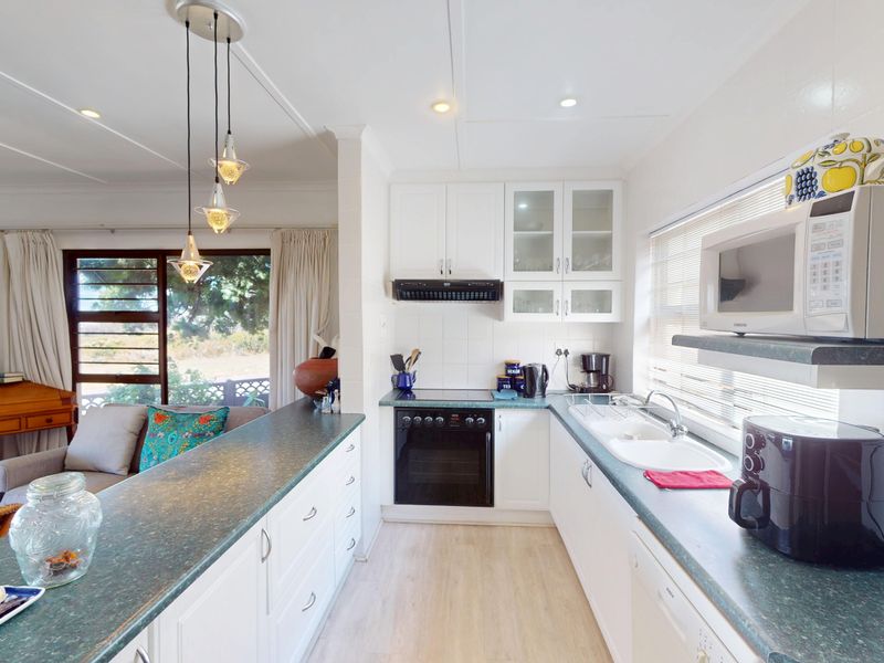 Open-plan kitchen featuring white cabinetry, green laminate countertops, built-in appliances, and a breakfast bar overlooking the adjacent living area.