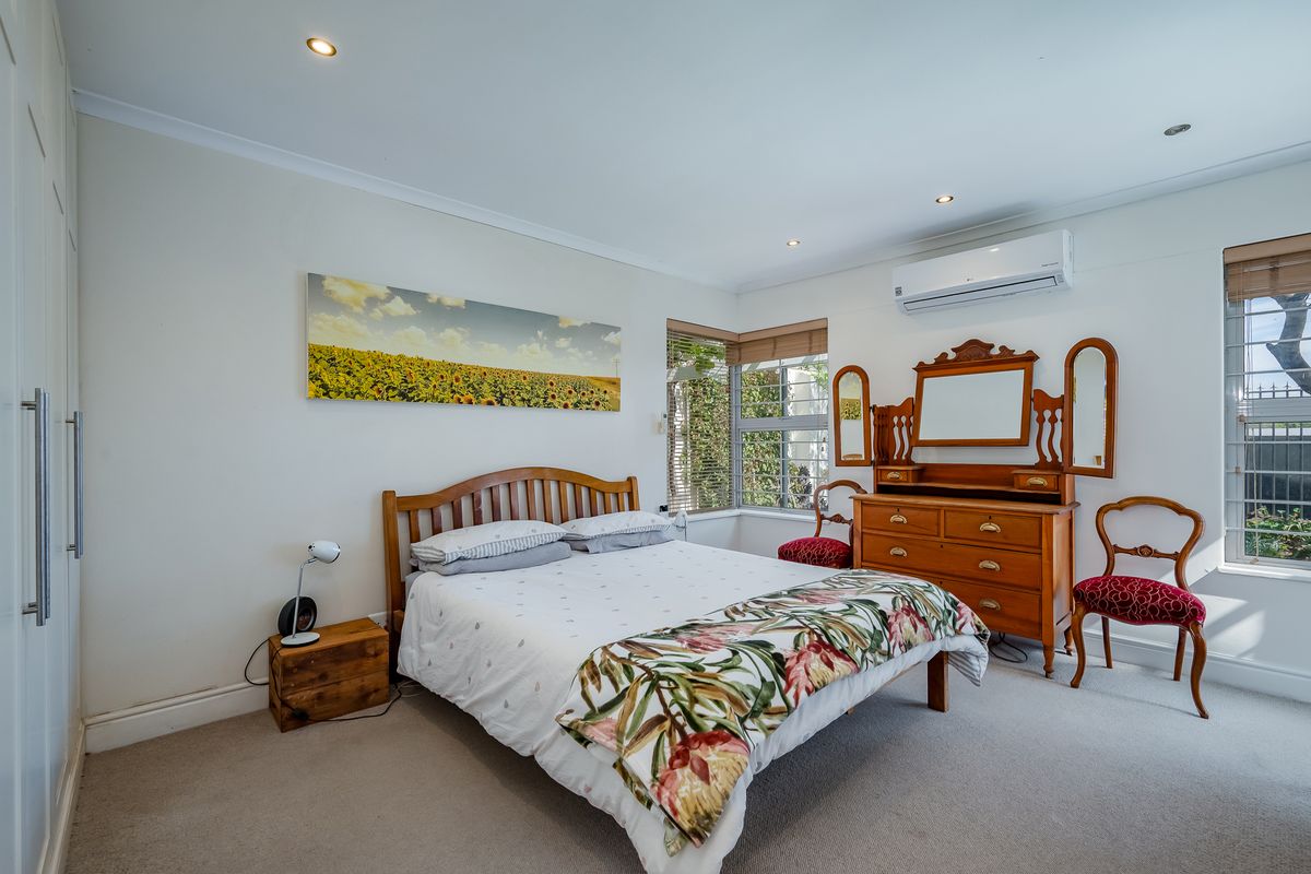 A well-maintained bedroom featuring neutral carpet, built-in storage, corner windows for natural light, and a wall-mounted split-system air conditioner.