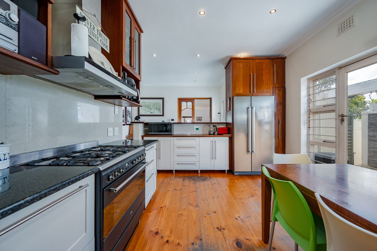A functional kitchen featuring timber flooring, white cabinetry, stone countertops, and a gas stove with an integrated extractor fan.