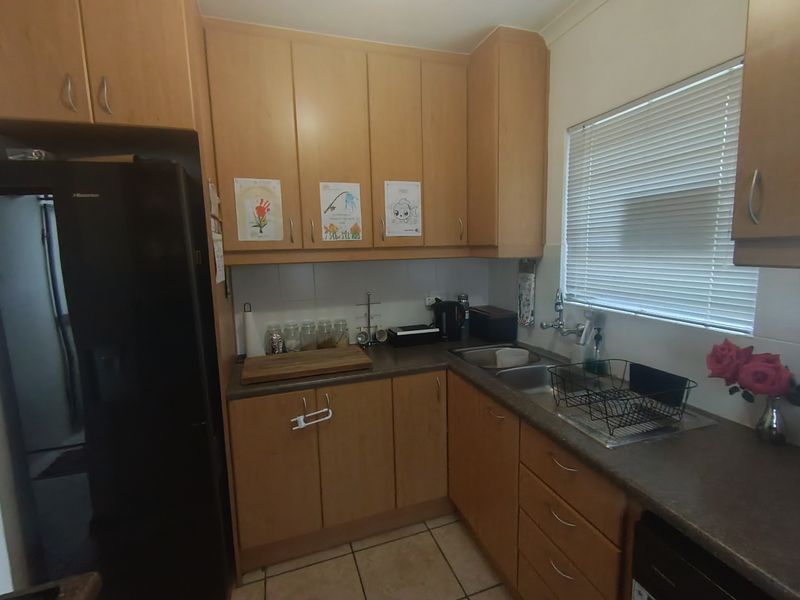 A functional kitchen featuring laminate cabinetry, laminate countertops, a double bowl stainless steel sink, and tiled flooring.