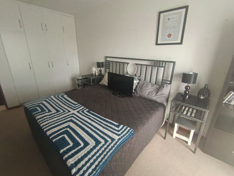 A bedroom featuring neutral walls, carpeted flooring, and ample storage provided by a set of built-in cupboards.