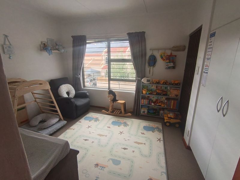 A functional bedroom featuring built-in cupboards, security bars on the window, and neutral finishes, suitable for a child's room or home office.