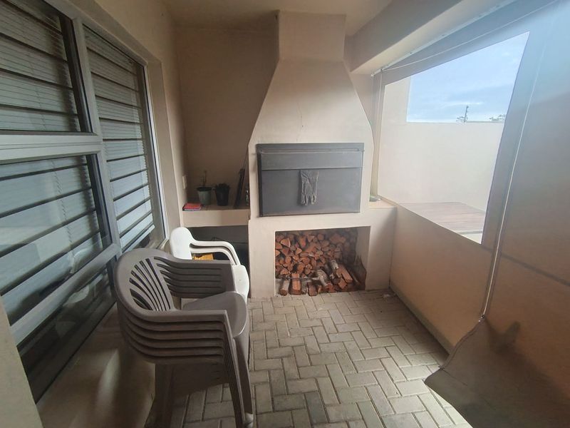Covered patio area featuring a built-in braai with integrated wood storage and brick paved flooring, offering a functional outdoor entertainment space.
