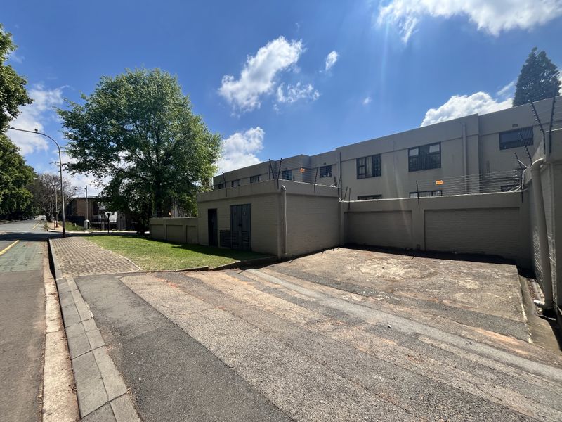 Exterior view of the apartment complex featuring a paved driveway, perimeter wall with electric fencing, and street-side access.
