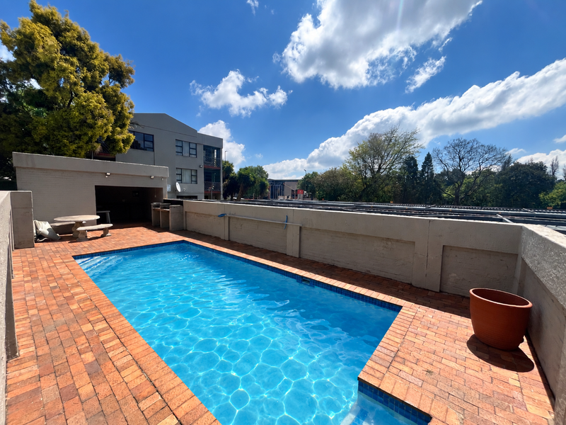 Outdoor pool area featuring a swimming pool, brick paved surround, and a built-in braai area set against a masonry boundary wall.