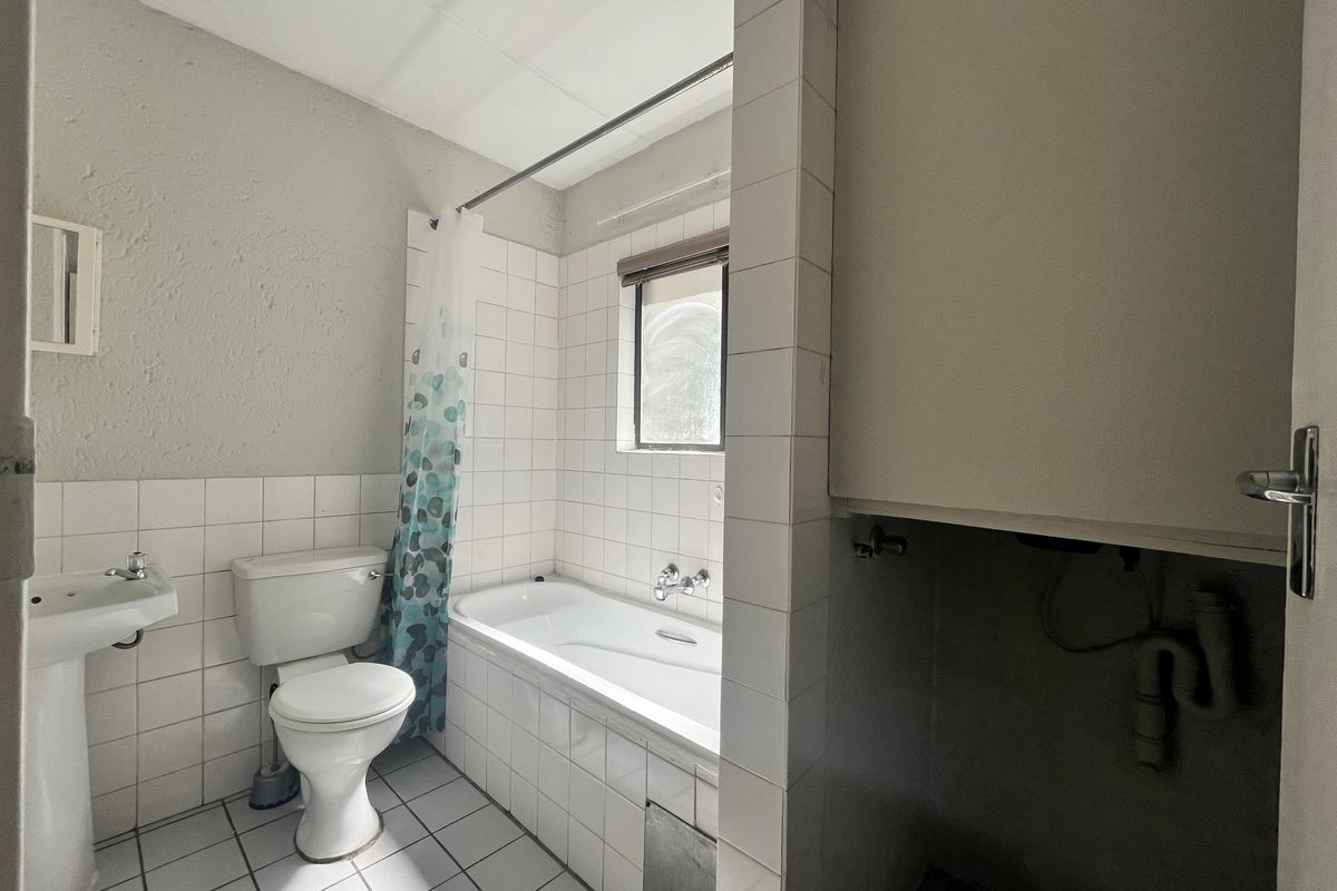 A functional bathroom featuring a pedestal basin, toilet, and bathtub with tiled finishes, requiring some cosmetic updates and repairs to the exposed plumbing area.