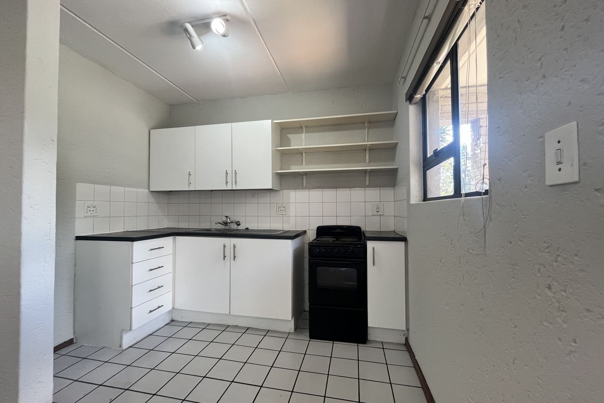 A functional kitchen featuring white built-in cabinetry, tiled backsplash, open shelving, and a freestanding stove, offering a clean and practical workspace.