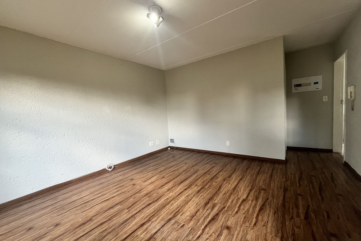 An empty living room featuring wood-look laminate flooring, neutral walls, and an integrated intercom system, providing a blank canvas for interior design.