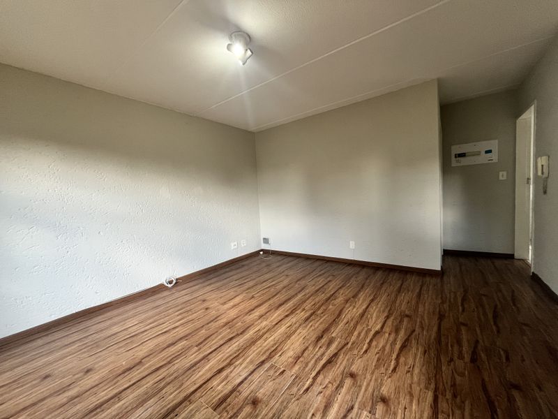 An empty living room featuring wood-look laminate flooring, neutral walls, and an integrated intercom system, providing a blank canvas for interior design.