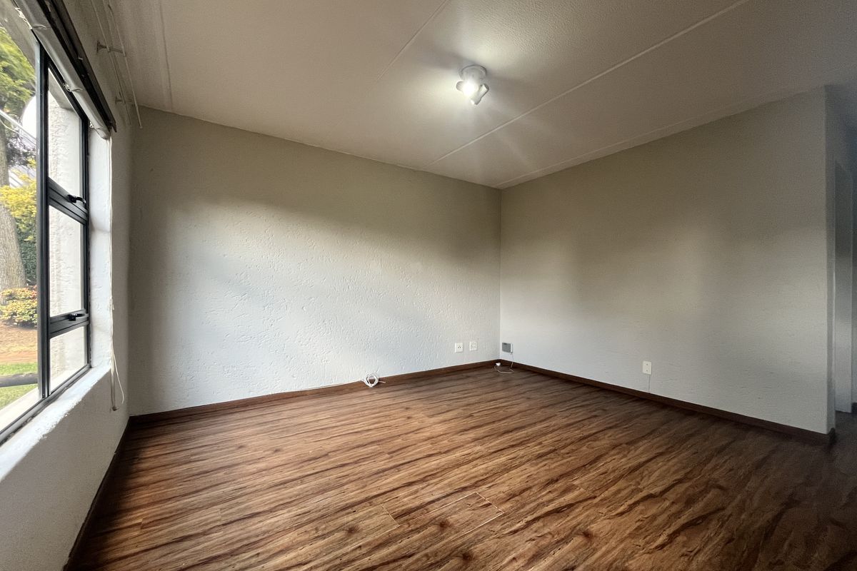 A bright, empty bedroom featuring wood-look laminate flooring, neutral walls, and a large window providing natural light.