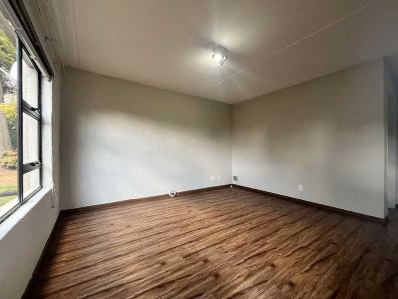 A bright, empty bedroom featuring wood-look laminate flooring, neutral walls, and a large window providing natural light.