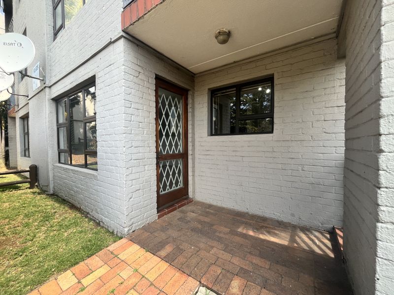 Exterior view of an apartment entrance featuring a brick facade, paved walkway, and a secure entrance door with a metal security gate.