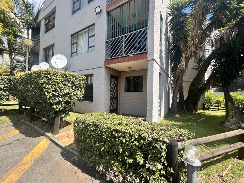 Front elevation of a multi-story apartment building featuring brick construction, a private balcony with security bars, and established garden landscaping.